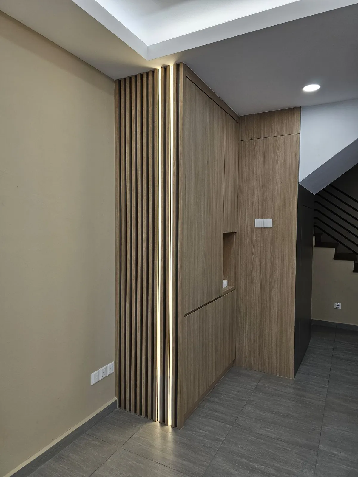 Taman Ara Permai wood-grain wall cabinetry with lit slats beside the staircase