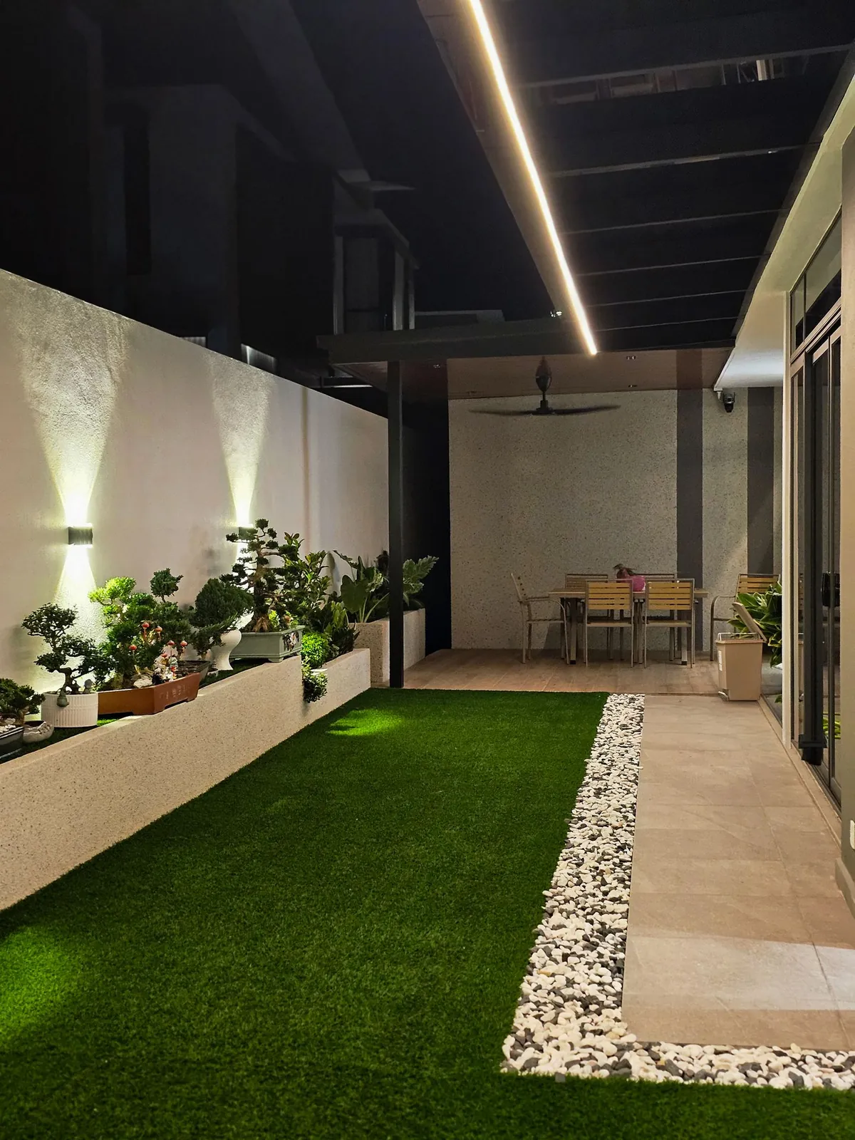 Side garden at night with turf, pebble strip and wall lights, Country Villa