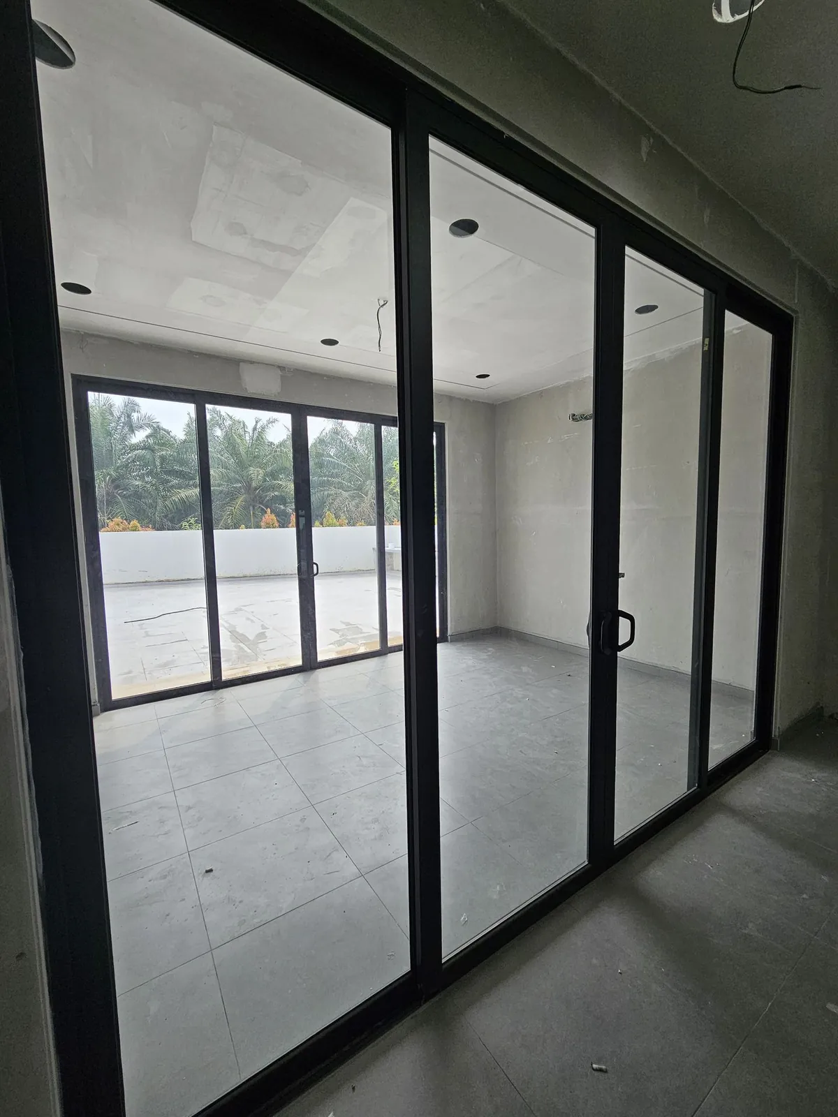 Jasin Parkland view through black-framed sliding doors into the tiled extension room